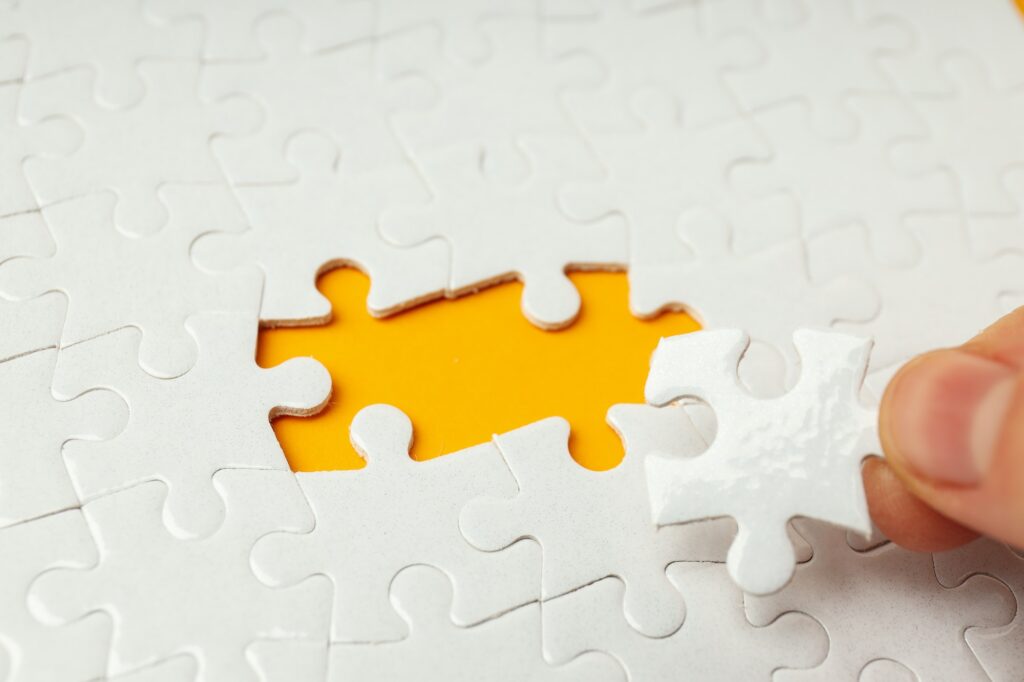 White puzzles without two puzzles on orange background and fingers hold puzzle